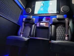 Blue-lit van conversion cabin showing captain chair and entertainment layout