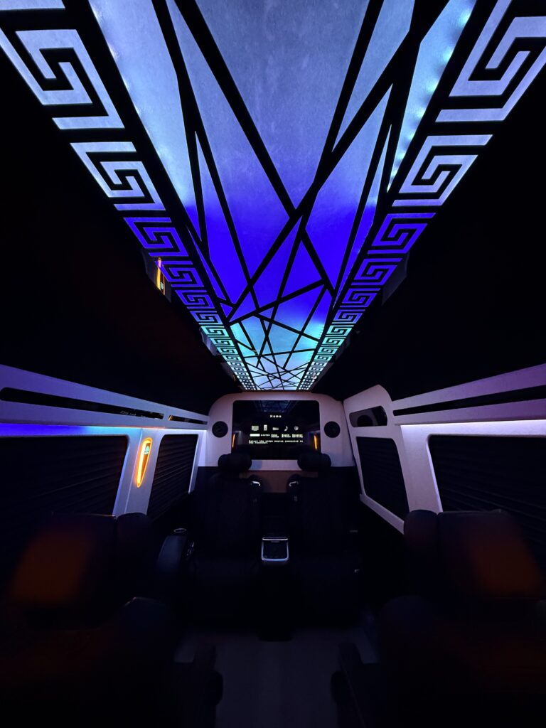 Diamond-quilted captain chairs beneath a geometric Greek-key ceiling panel in a custom van conversion