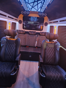 Wide view of a custom van conversion cabin with geometric ceiling design and entertainment display