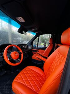 Orange leather steering wheel and captain chair in a custom Mercedes Sprinter van conversion
